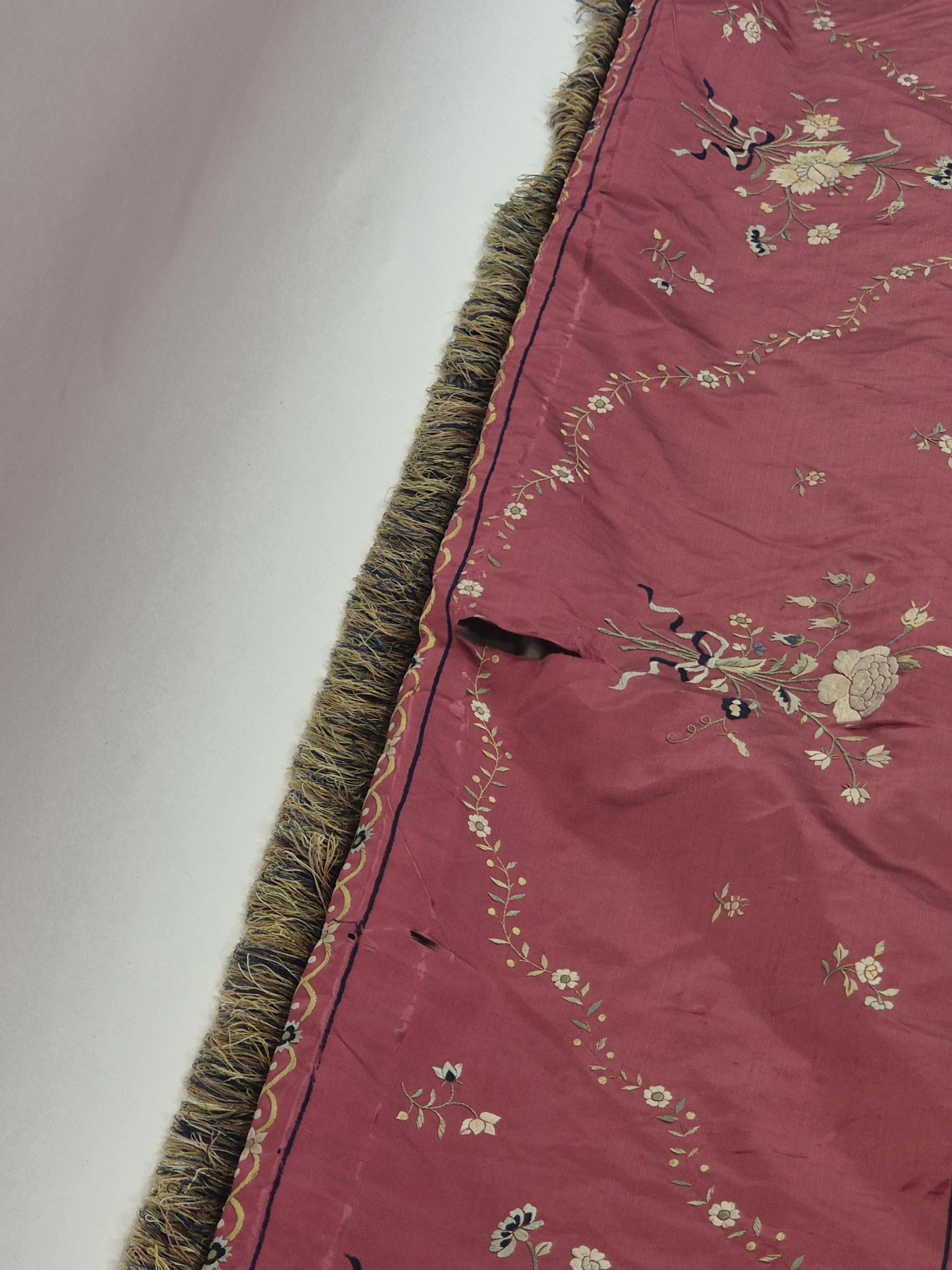 A Chinese 19th century Qing Dynasty crimson red silk embroidered hanging. Embroidered with sprays and swags of flowers and foliage, depicting prosperity and fortune, around a central stylistic sun motif, depicting perfec